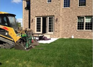 backhoe on a lawn outside of a brick house